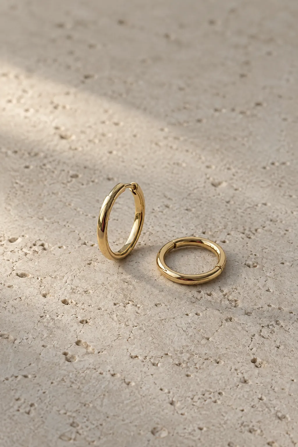 A pair of small plain gold hoops on pale limestone.