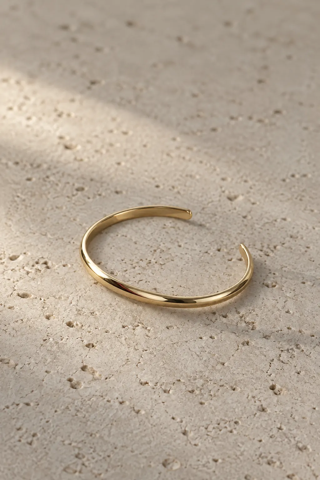 A slim open gold cuff on pale limestone.
